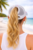 Back view of woman at the beach wearing Beach Please tie-dye trucker hat with ponytail through high opening - Crabby Mermaid