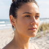 Woman wearing sterling silver wave drop earrings on the beach with ocean waves and sea oats in the background — Crabby Mermaid