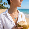 Woman wearing sterling silver ocean wave necklace with Swarovski crystals on the beach in a white linen shirt holding a coconut - handcrafted in Ireland - Crabby Mermaid
