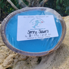 Spring showers coconut shell candle resting on rock outdoors — all natural blue soy coconut wax candle — Crabby Mermaid