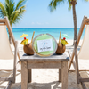 Lime in the coconut shell candle on beach table between two lounge chairs with tropical coconut drinks and palm trees — Crabby Mermaid