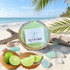 Lime in the coconut half shell coconut candle on sandy beach with fresh limes split coconut driftwood and sea glass — Crabby Mermaid