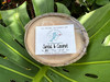 Santal and coconut half shell coconut candle with Crabby Mermaid label resting on monstera leaf — all natural soy coconut wax — 5.5 oz