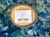 Santal and coconut half shell coconut candle on blue sea glass rocks — all natural soy coconut wax candle — Crabby Mermaid