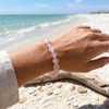 Woman wearing rose quartz beaded stretch bracelet at the beach with shells and driftwood — Crabby Mermaid