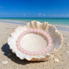 Rose quartz gemstone bracelet resting in a seashell on a Florida Gulf Coast beach