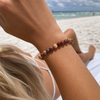 Woman wearing mookaite gemstone beaded bracelet on her wrist while relaxing on a Florida beach