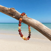 Mookaite gemstone bracelet hanging on driftwood with turquoise water in the background