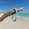 White howlite gemstone beaded stretch bracelet hanging from driftwood on a Florida Gulf Coast beach