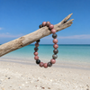Black stripe rhodonite gemstone bracelet hanging from driftwood on a Florida Gulf Coast beach