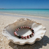 Black stripe rhodonite gemstone bracelet laying inside a seashell on a Florida Gulf Coast beach