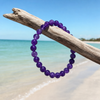 Amethyst gemstone beaded stretch bracelet hanging from driftwood on Florida Gulf Coast beach — deep purple natural amethyst beads — Crabby Mermaid