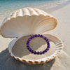 Amethyst gemstone beaded stretch bracelet in open seashell on Florida Gulf Coast beach — deep purple 8mm natural amethyst beads — Crabby Mermaid