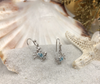 Sterling silver crab drop earrings with aqua blue Swarovski crystals displayed on seashell and sand — Irish coastal jewelry