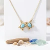 Yellow gold plated Larimar two turtle necklace displayed on white card with driftwood shells and sea glass - Crabby Mermaid