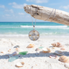 Sterling silver mother of pearl compass necklace hanging from driftwood at Florida Gulf Coast beach with shells and sea glass - Crabby Mermaid