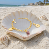 Interchangeable charm bracelet in 14K gold with tourmaline charms in seashell on Florida Gulf Coast beach — Crabby Mermaid