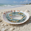 Stone Wrap Blue Howlite Gold coiled in a seashell on a white sand Florida Gulf Coast beach — Crabby Mermaid