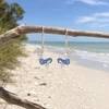 Sterling silver sapphire blue crystal mermaid earrings hanging from driftwood on Florida beach - handcrafted in Ireland - Crabby Mermaid