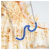 Close-up of sterling silver sea wave necklace with sapphire blue Swarovski crystals resting on seashell - handcrafted in Ireland - Crabby Mermaid