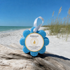 Spongellé Freesia Pear Wild Flower buffer on driftwood at Florida Gulf Coast beach with sea oats and turquoise water - Crabby Mermaid