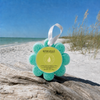 Spongellé Coconut Verbena Wild Flower buffer on driftwood at Florida Gulf Coast beach with sea oats and turquoise water — Crabby Mermaid