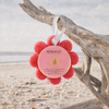 Spongellé Grapefruit Cassis Wild Flower buffer hanging by white ribbon from driftwood on Florida Gulf Coast beach - Crabby Mermaid