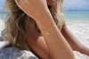 Model wearing 18K gold paperclip charm keeper bracelet with CZ mermaid tail charm on Florida Gulf Coast beach - Crabby Mermaid
