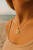 Model wearing gold epoxy starfish disc charm necklace on Singapore chain — close-up neckline shot at beach