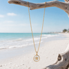 Gold epoxy starfish charm necklace hanging from driftwood on Florida Gulf Coast beach — waterproof coastal jewelry