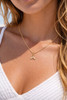 Model wearing gold CZ mermaid tail charm necklace on Singapore chain — close-up neckline shot at beach