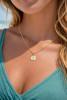 Model wearing gold epoxy seahorse disc charm necklace on Singapore chain - close-up neckline shot at beach