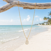 Gold epoxy seahorse charm necklace hanging from driftwood on Florida Gulf Coast beach - waterproof coastal jewelry