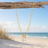 Gold 18K PVD paperclip necklace with pearl and seahorse charms draped over driftwood on Florida Gulf Coast beach - Crabby Mermaid