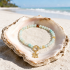 18K gold PVD amazonite bead bracelet with sea turtle charm resting in a seashell on a white sand Florida Gulf Coast beach