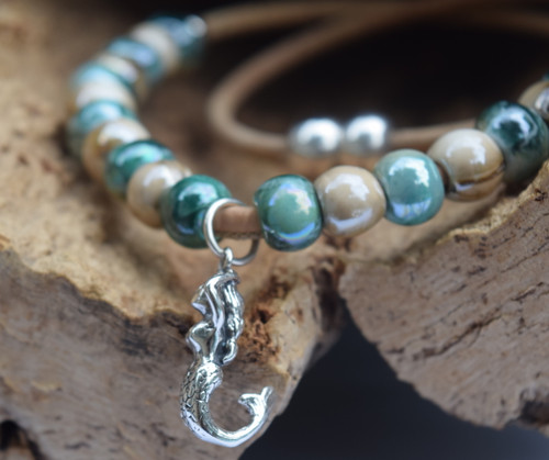 Close-up of sterling silver mermaid charm on glazed teal and beige ceramic bead cork necklace — handcrafted in Florida