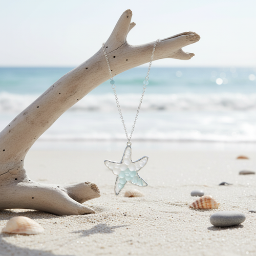 Sea glass starfish pendant necklace hanging from driftwood with ocean waves in background - coastal jewelry - Crabby Mermaid