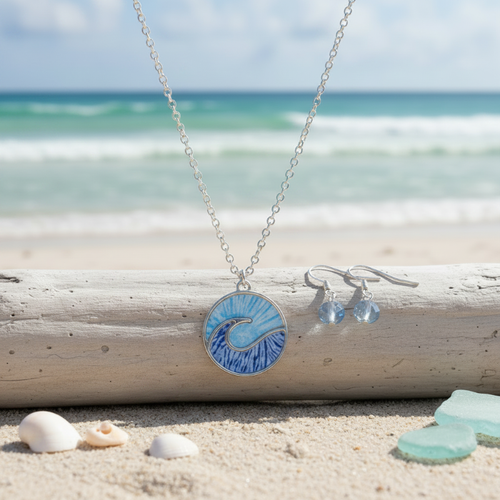 Blue enamel wave necklace and crystal earring set resting on driftwood with shells and sea glass on sandy beach - coastal jewelry set - Crabby Mermaid