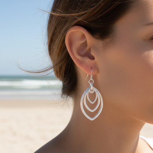 Burnished silver triple marquise hoop earrings worn on model's ear with sandy beach and ocean in background - coastal jewelry - Crabby Mermaid