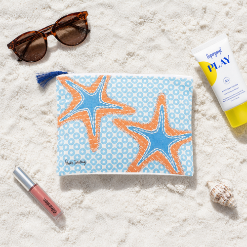 Starfish cotton cosmetic bag laying flat on white Florida beach sand surrounded by sunglasses, sunscreen, and a seashell — Crabby Mermaid