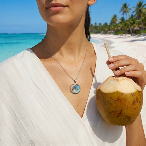 Woman wearing sterling silver ocean wave necklace with Swarovski crystals on tropical beach holding coconut - handcrafted in Ireland - Crabby Mermaid