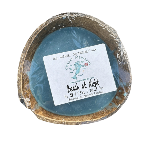 Beach at night coconut shell candle with driftwood and sand on dark navy background — natural soy coconut wax candle — Crabby Mermaid