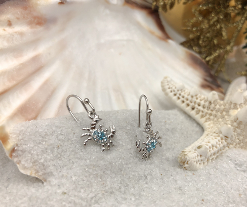Sterling silver crab drop earrings with aqua blue Swarovski crystals displayed on seashell and sand — Irish coastal jewelry