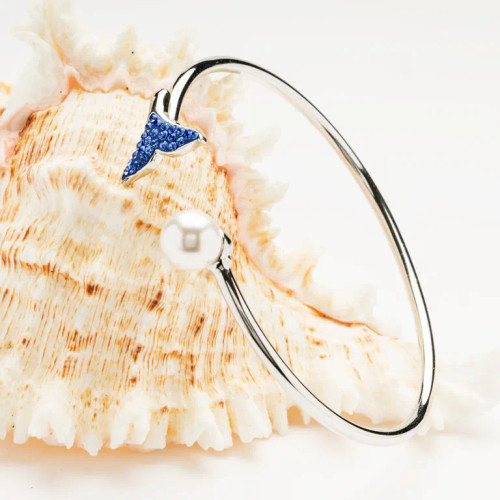 Discover joy and good fortune with our Ocean’s Sterling Silver Pearl Whale Tail Bangle, featuring sapphire crystals and a freshwater pearl. Shop coastal-inspired jewelry at crabbymermaid.com.