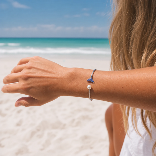Sterling silver whale tail cuff bangle with sapphire crystals and freshwater pearl worn on model at Florida beach ‚Äî handcrafted in Ireland ‚Äî Crabby Mermaid