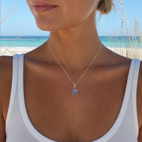 Sterling silver sapphire blue starfish necklace with crystal accents worn by sandy blonde model on Florida beach - handcrafted in Ireland - Crabby Mermaid