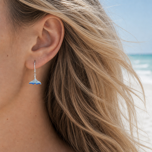 Model wearing sterling silver whale tail drop earrings with ombre blue crystals at Florida Gulf Coast beach - handcrafted in Ireland - Crabby Mermaid