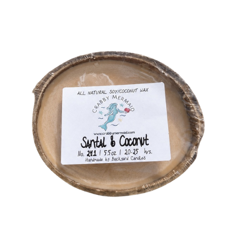 Santal and coconut half shell coconut candle with Crabby Mermaid label resting on tree stump outdoors — all natural soy coconut wax — 5.5 oz