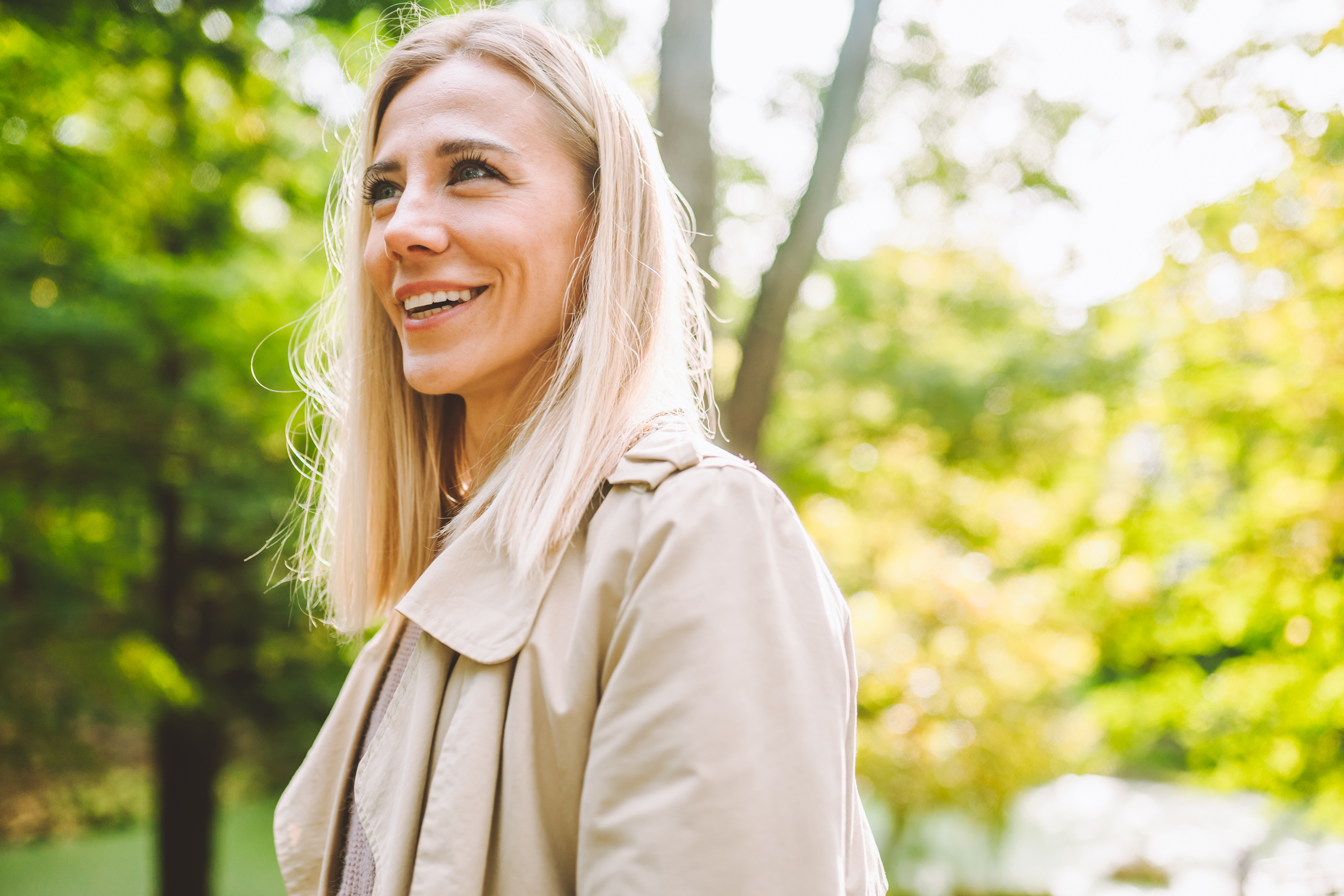 Smiling blonde woman standing outside looks happily to the side.