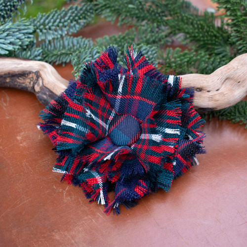 Close-up of handmade tartan rosette brooch featuring red, blue, and green plaid fabric.
